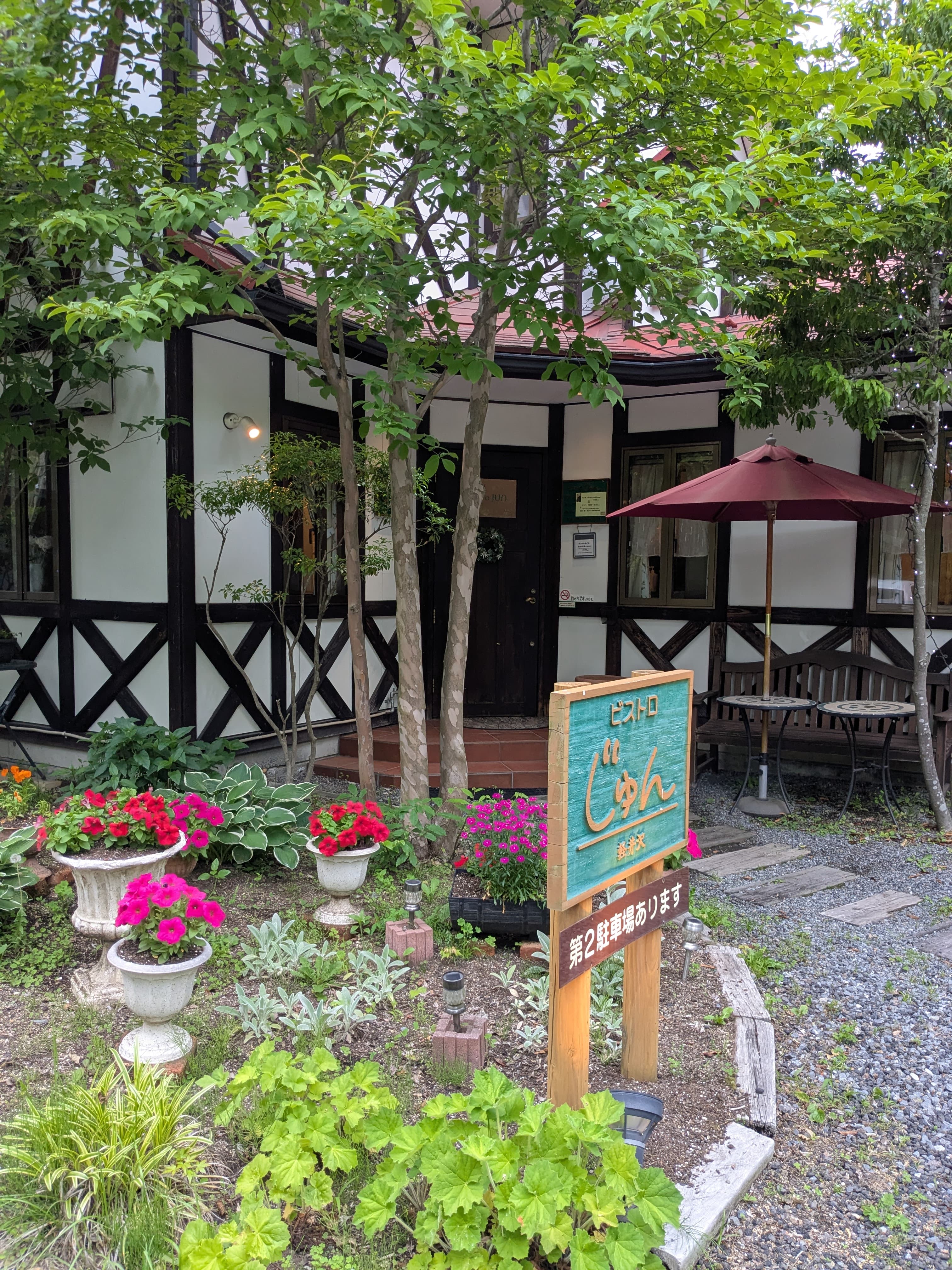 軽井沢塩沢のビストロじゅん外観。白壁に黒のハーフティンバー、赤いパラソル、花壇。